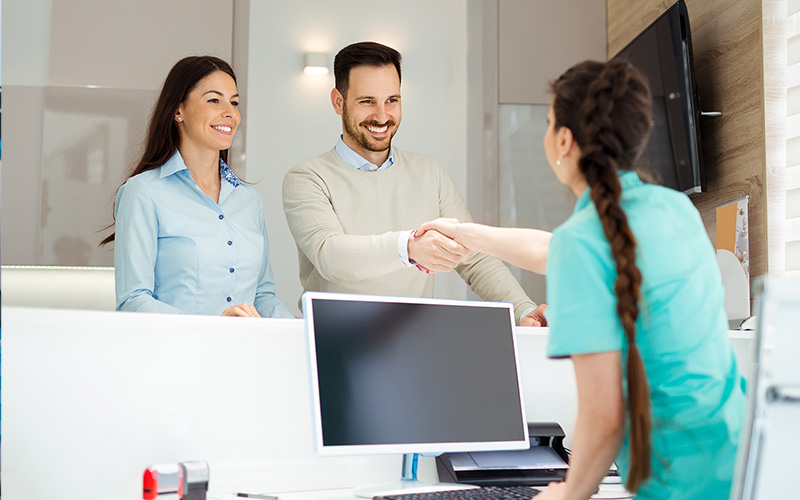 The image shows three individuals in an office environment a man and woman shaking hands with another person who appears to be receiving the handshake, suggesting a formal greeting or agreement being made.