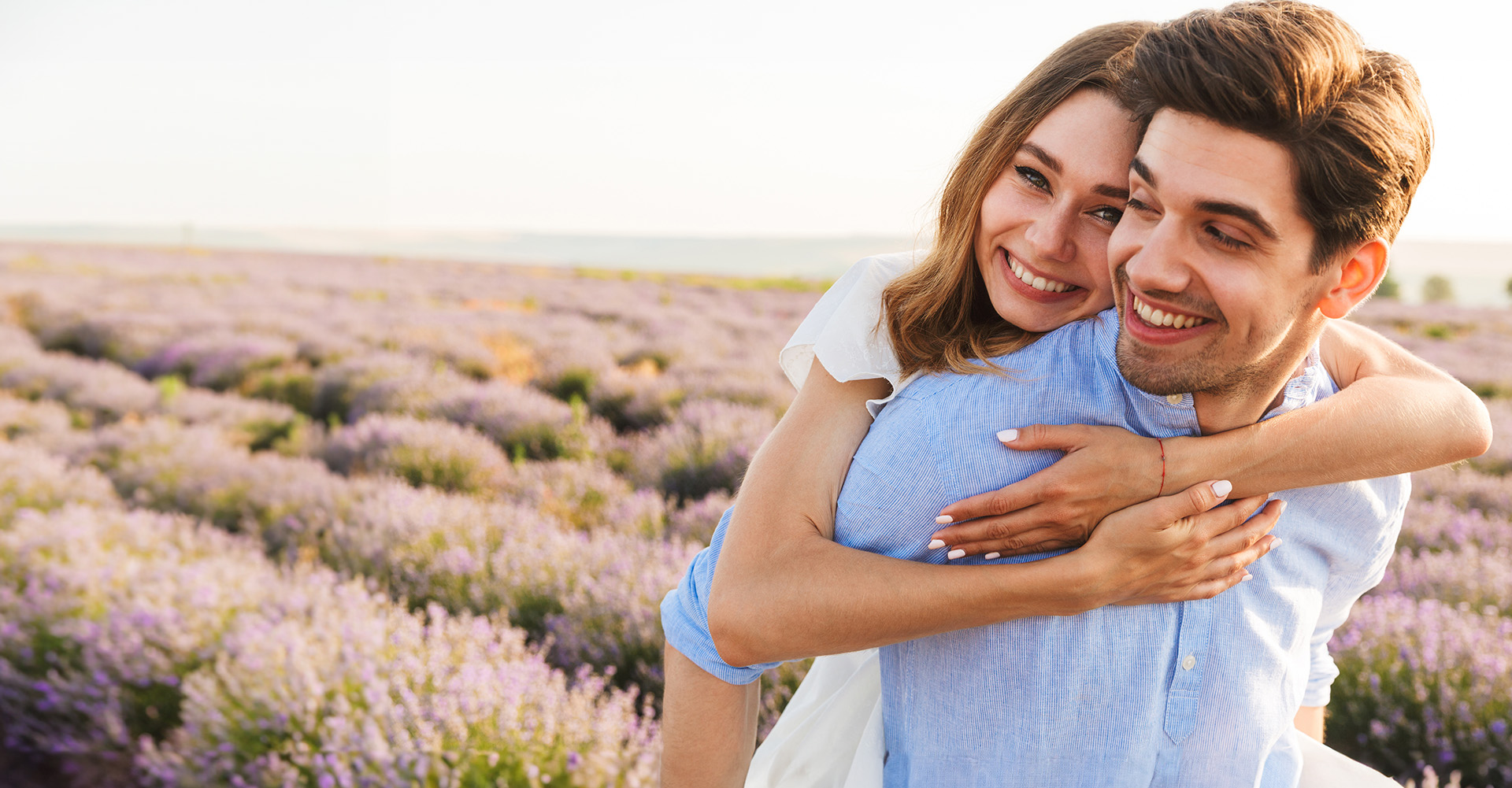 The image shows a man and woman embracing each other in an outdoor setting with lavender fields in the background.